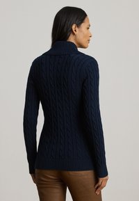 Ναυτικό μπλε πλεκτό πουλόβερ με καλωδιωτές λεπτομέρειες, ψηλό γιακά και ραμμένα μανίκια. Υφασμάτινη υφή σε εφαρμοστή σιλουέτα με μακριά μανίκια.