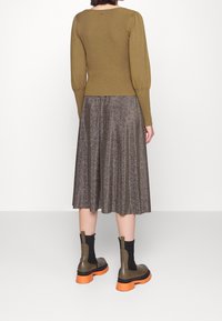 Olivenfarbener Rippstrickpullover mit puffigen Ärmeln, kombiniert mit einem knielangen, metallisch bronzefarbenen, plissierten Rock und klobigen, olivgrünen und orangefarbenen Stiefeletten.