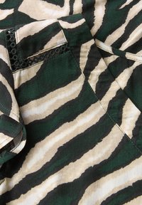 Tessuto a strisce zebrate in verde e beige. Materiale di cotone con una texture liscia. Include una tasca e dettagli di cucitura decorativa.