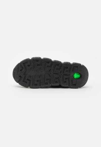 Black rubber shoe sole with textured grip, featuring a geometric pattern and a green accent detail near the heel.