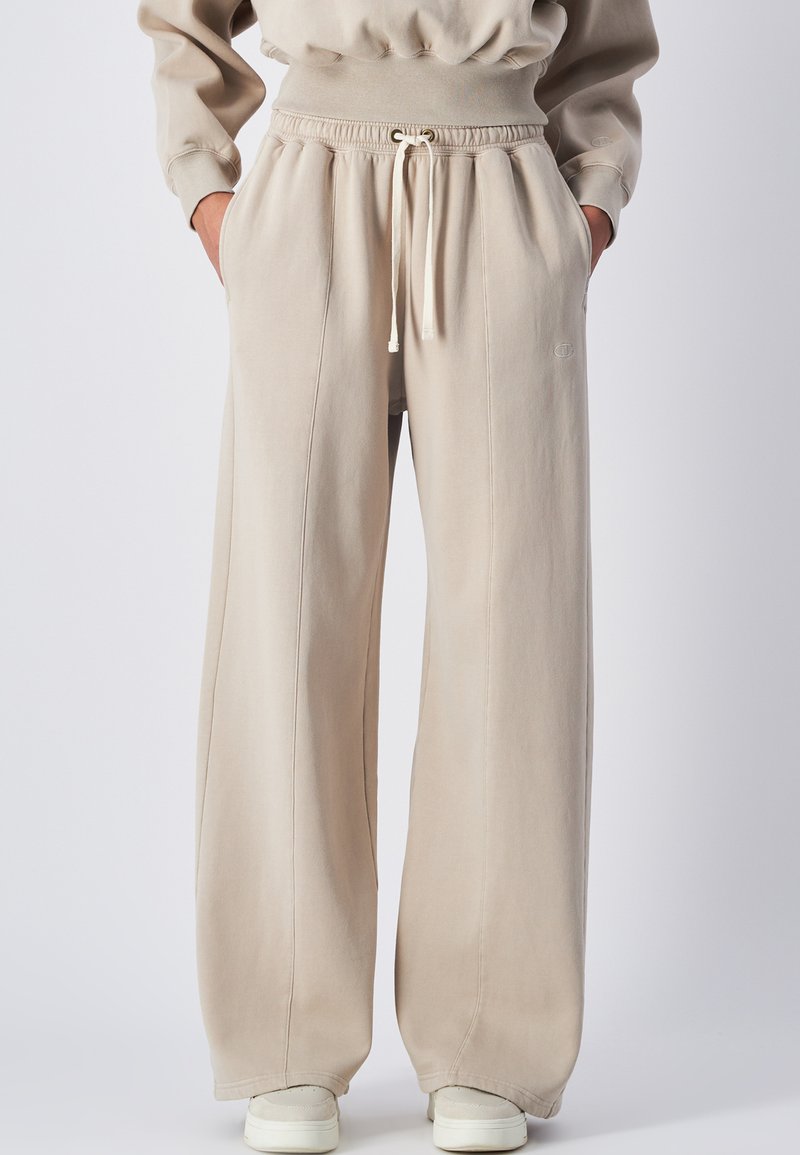 Pantaloni della tuta larghi beige realizzati in morbido misto cotone, con vita elastica e cordoncino, tasche laterali e dettagli cuciti.