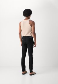 Beige ribbad toppi, mustat slim-fit farkut, sandaalit. Hoikka siluetti, sileä pinta ja vähäiset yksityiskohdat molemmissa vaatteissa.