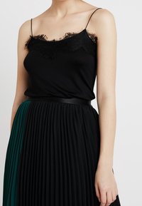 Svart ärmlös linne med spetsdetaljer, parat med en plisserad svart och grön kjol med svart midjeband.