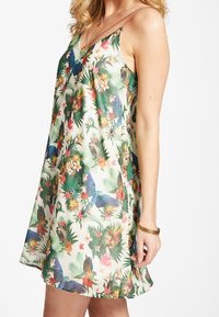 Ärmelloses, mehrfarbiges Kleid mit einem tropischen Druck, der Vögel, Blumen und Laub auf einem hellen Hintergrund zeigt; glattes Material, lockere Passform.