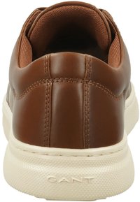 Braune Leder-Sneaker mit glatter Oberfläche, gepolstertem Kragen und einer kontrastierenden cremefarbenen Gummisohle. Genähte Details entlang des Obermaterials.