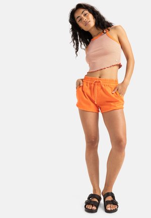 Stripped crop top with orange and white lines, frilled hem; orange shorts with elastic waist, side pockets; black sandals with two buckles.