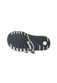 Suola delle scarpe di colore grigio scuro con dettagli bianchi, caratterizzata da strisce orizzontali per la trazione e un logo circolare. Superficie testurizzata per una migliore aderenza.