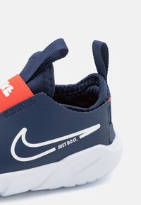 Marinblå sko med ett texturerat tygöverdrag, röd accent vid hälen och vit logotyp med texten "JUST DO IT" på sidan; segmenterad vit sula.