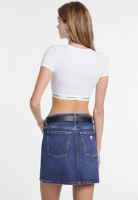 Witte cropped t-shirt met korte mouwen en een logo band aan de onderkant, gecombineerd met een donkerblauwe denimrok met twee achterzakken.