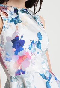 Robe florale avec un corsage ajusté et une jupe évasée, présentant des teintes de bleu, rose et violet sur un fond clair. Fabriquée en tissu lisse et doux.