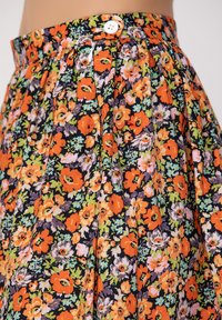 Jupe fleurie avec un fond noir, ornée de fleurs orange vif, roses et vertes. Design plissé avec une fermeture à bouton à la taille.