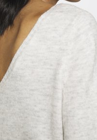 Jasnoszary sweter dziany z głębokim dekoltem w kształcie litery V i teksturowanym wykończeniem, ukazujący miękkość materiału oraz skomplikowany wzór dzianiny.