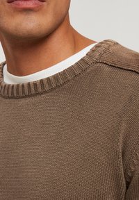 Br�ązowy sweter z dzianiny z prążkowanym dekoltem. Tekstura jest miękka i równa, z warstwowym wyglądem, z białą koszulą pod spodem.