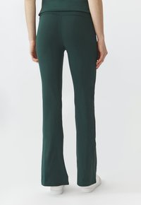 Ausgestellte Yogahosen in Dunkelgrün, aus elastischem Stoff. Sie verfügen über einen taillierten Bund und eine glatte Textur, kombiniert mit weißen Sneakers.