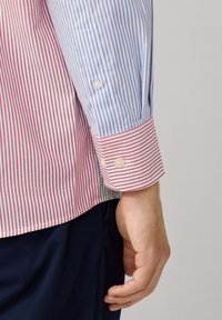 Camisa a rayas con franjas alternas rojas y azules, con puños abotonados y un corte entallado. La tela parece suave y tiene un ligero brillo.