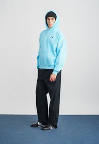 Himmelblå huvtröja med framficka, svart logotyp, löst sittande svarta byxor och svarta träningsskor med vita detaljer.