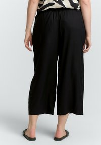 Culottes negros de pierna ancha con una cinturilla elástica, confeccionados en una tela ligera, que cuentan con una textura suave y un corte a la altura del tobillo.