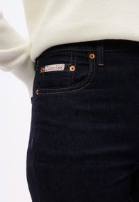 Σκούρο μπλε τζιν παντελόνι με χαλκόχρωμες λεπτομέρειες, που διαθέτει ετικέτα Calvin Klein στην μπροστινή τσέπη και χρυσές ραφές.