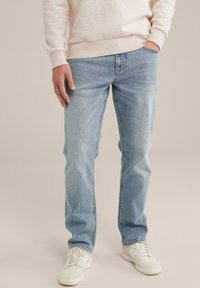 Šviesiai mėlynos džinsinės kelnės su tiesiu kirpimu, pasižyminčios priekinėmis kišenėmis, subtiliu siuvinėjimu ir dėvėtu audiniu. Derinama su baltomis sportbačiais.