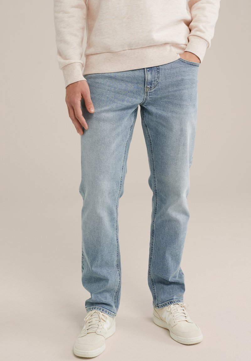 Šviesiai mėlynos džinsinės kelnės su tiesiu kirpimu, pasižyminčios priekinėmis kišenėmis, subtiliu siuvinėjimu ir dėvėtu audiniu. Derinama su baltomis sportbačiais.