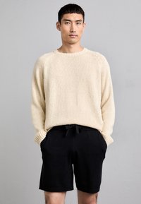 Beige strikket sweater med struktureret overflade, parret med sorte shorts med elastisk talje og sidelommer.