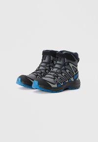 Chaussures de randonnée noires et grises avec des accents bleus, dotées d'un dessus texturé, de bandes réfléchissantes et de semelles robustes pour l'adhérence.