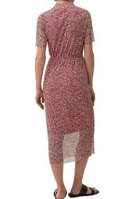 Vestido largo de patrón floral rojo con mangas cortas, cintura ceñida, sección inferior transparente y detalle de ojal en la espalda. Sandalias planas negras.