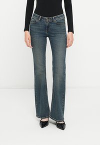 Bukser i blå denim med vidde, klassisk passform, fem lommer og metallknaplukning. Stoffet har en jevn tekstur med subtil falming.