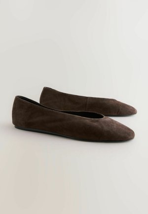 Brune ruskind flats med spidse tæer, vist mod en neutral baggrund, der fremhæver deres elegante og minimalistiske stil.