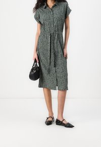 Vestito midi verde con stampa leopardata, maniche corte e chiusura a bottoni davanti. Abbinato a ballerine nere e una piccola borsa nera.