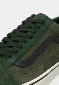 Dark green suede sneakers feature matching laces, a black leather side stripe, and a thick white rubber sole with subtle stitching details.