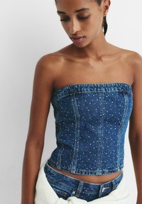 Top din denim albastru fără bretele, cu panouri cusute și embellishments. Design scurt cu o siluetă conturată și detalii cu margine brută.