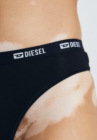 Fekete pamut bikini széles derékpánttal, ami fehér "DIESEL" felirattal van ellátva. Simaszerkezetű, tiszta élekkel és látható minták nélkül.
