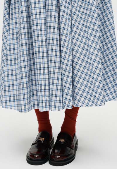 Μπλε και λευκή καρώ φούστα συνδυασμένη με σκουρόχρωμες κάλτσες σε χρώμα σκουριάς και μαύρα δερμάτινα μοκασίνια με χρυσές διακοσμήσεις.
