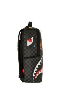 Zaino a scacchi nero con design di bocca di squalo, dettagli rossi e denti bianchi, tasca laterale e maniglia superiore.