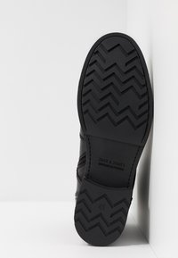 Suela de zapato de cuero negro con un patrón texturizado en forma de zigzag. Presenta una marca en relieve y un tamaño 41. Diseño minimalista con un acabado mate.