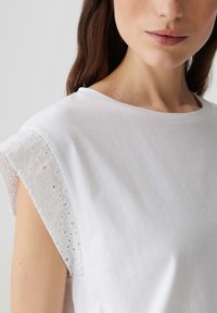 Witte katoenen top met korte, kanten mouwen. Eenvoudig ontwerp met een ronde halslijn en een gladde textuur. Geen zichtbare patronen of accenten.