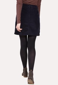 Marineblaue Cordmini mit geradem Schnitt, subtiler Textur, getragen mit schwarzen Strumpfhosen und grauen Stiefeletten, von hinten betrachtet.