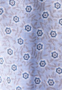 Tissu bleu clair avec de petits motifs floraux bleu foncé et blanc dispersés uniformément sur une surface texturée.