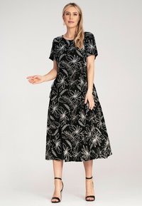 Black dress featuring white floral patterns, short sleeves, and a knee-length A-line silhouette. Smooth texture. Worn with black strappy heels.