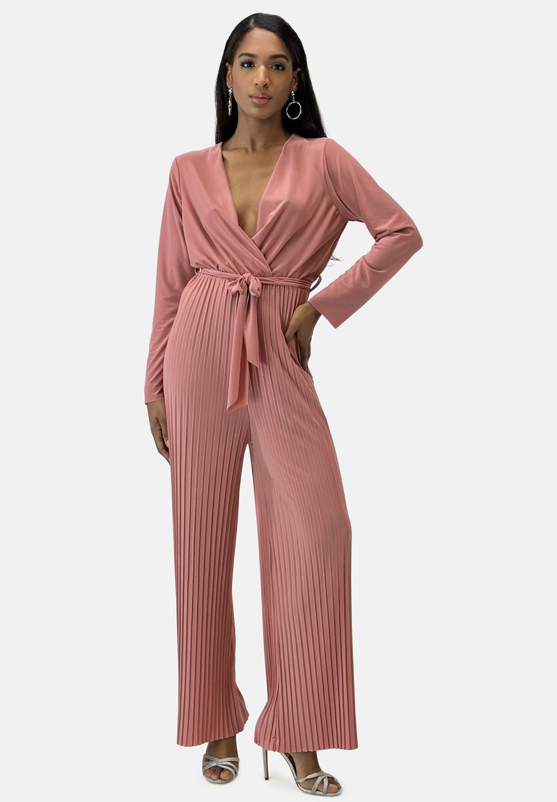 Tuta color rosa con maniche lunghe, scollatura a V profonda, tessuto plissettato e vita con fiocco. Presenta tasche laterali e un design ampio e fluido.