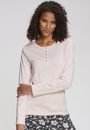 Lichtroze longsleeve shirt met een ronde halslijn en een knoopsluiting met vijf knopen. Zacht materiaal; het model draagt bloemenpatroon broeken.