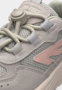 Uzumak blizu svijetlosivih i ružičastih tenisica od mrežaste tkanine, s antilop preklopcima, elastičnim vezicama i kopčom na jeziku.