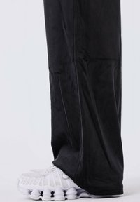 Zwarte joggingbroeken van stof met een gladde textuur, gecombineerd met witte sportschoenen met een bubbelzoolontwerp en netaccenten.