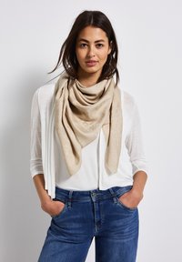 Beige sjaal met een subtiel patroon, om de hals gedrapeerd. Draag over een witte top en blauwe jeans, die een casual outfit toont.