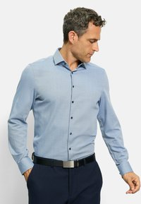 Hellblaues Button-Up-Hemd mit dezentem Muster, langen Ärmeln, Kragen und dunkelblauen Knöpfen. Getragen mit dunkler Hose und einem schwarzen Gürtel.