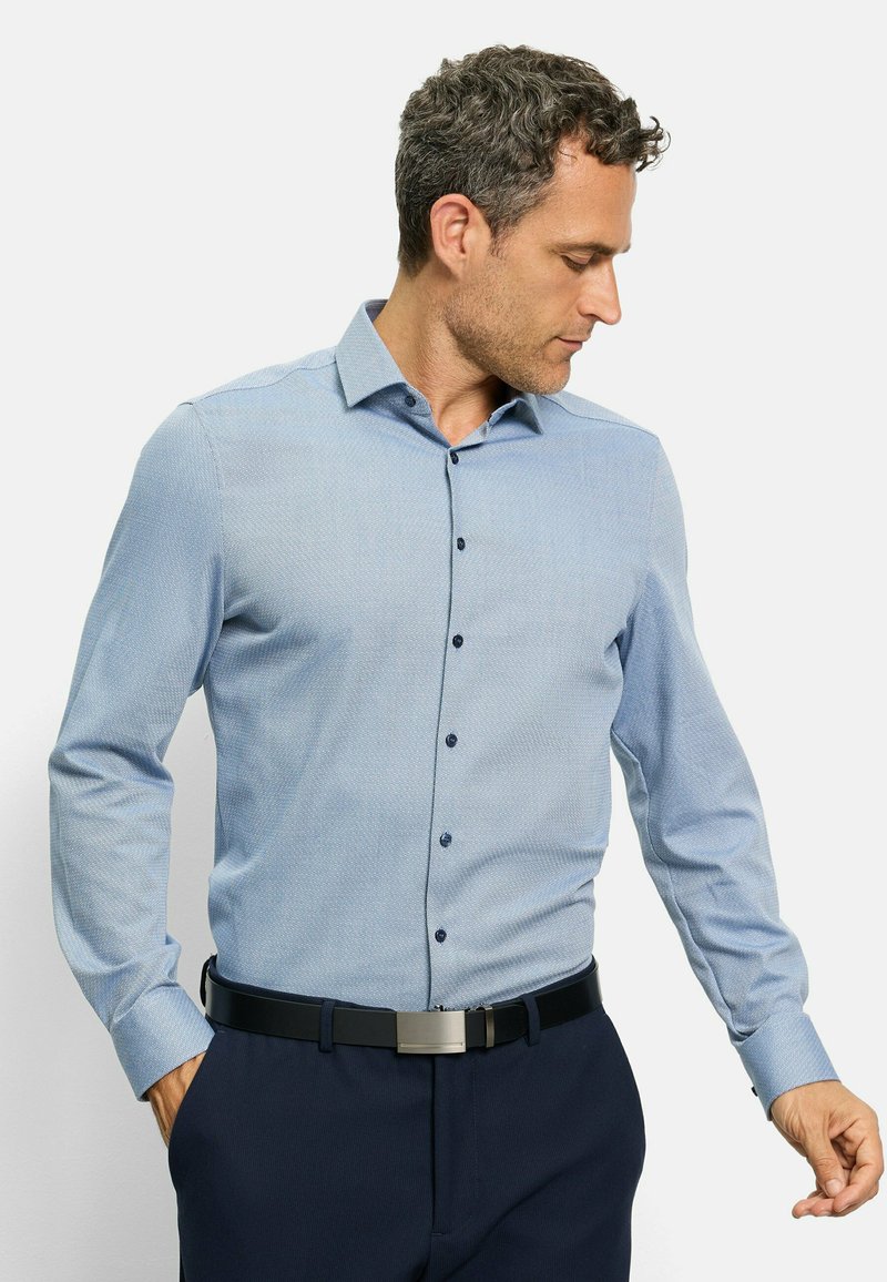 Hellblaues Button-Up-Hemd mit dezentem Muster, langen Ärmeln, Kragen und dunkelblauen Knöpfen. Getragen mit dunkler Hose und einem schwarzen Gürtel.