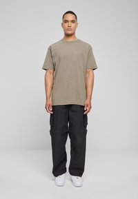 Camiseta de algodón verde oliva con cuello redondo, combinada con pantalones cargo negros que tienen bolsillos y puños ajustables. Zapatillas blancas.