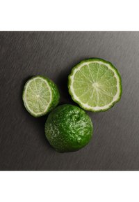 Groene limoenen gerangschikt op een textuurrijke donkere achtergrond. Een hele limoen en twee gehalveerde limoenen tonen een glanzende schil en een felgroene, sappige binnenkant.