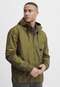 Olive green hooded jacket made from a lightweight material; features zip front, elastic cuffs, and a small logo patch on the chest.